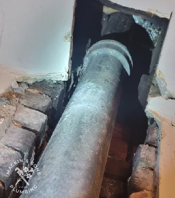 Corroded 4-inch cast iron drain stack exposed behind red brick in a Barberton basement wall