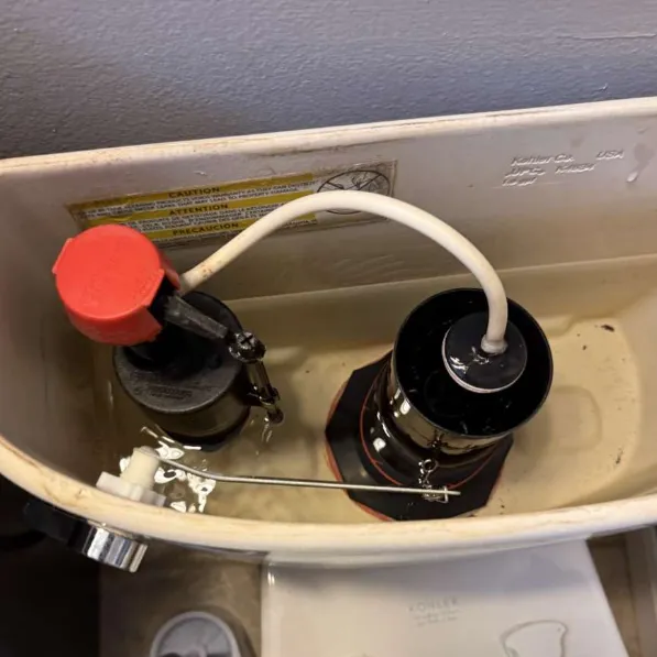 Inside a Kohler toilet tank showing the red-capped fill valve and the black flush valve