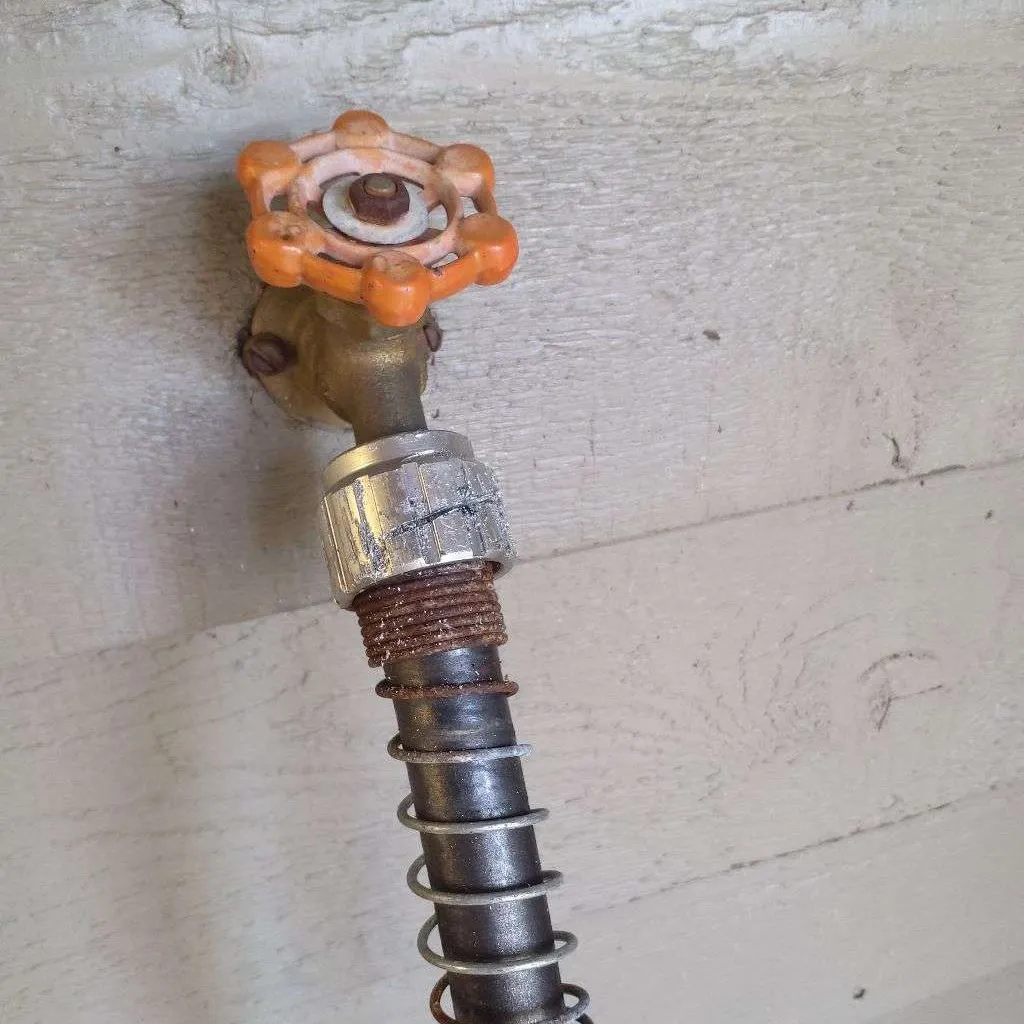 Brass outdoor hose faucet with an orange handle and a metal garden hose coupling seized onto its threads