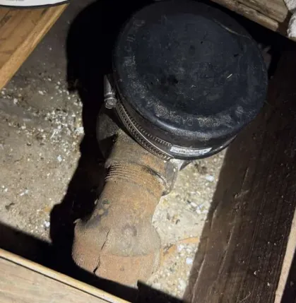 Original drum trap under the bathtub of a Norton home, rusted piping sealed with a rubber cap