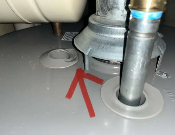 Arrow pointing to the plastic collar beside the draft hood on top of a gas water heater, where backdrafting exhaust melts the plastic
